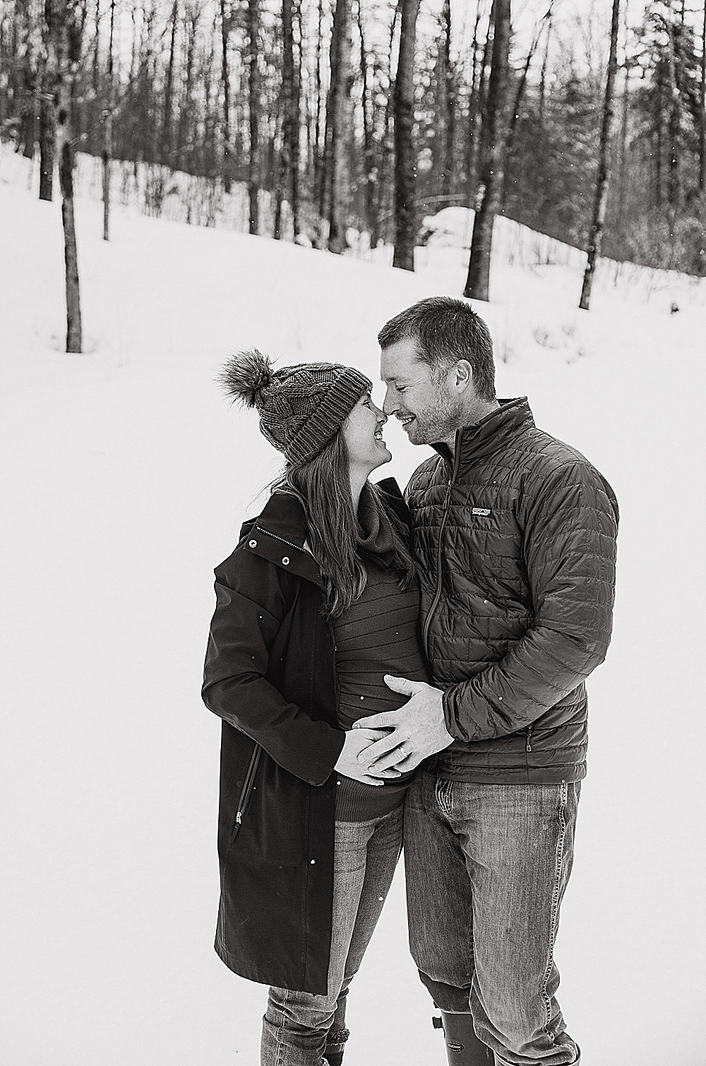 husband and wife with their hands on her baby bump, standing in the snow