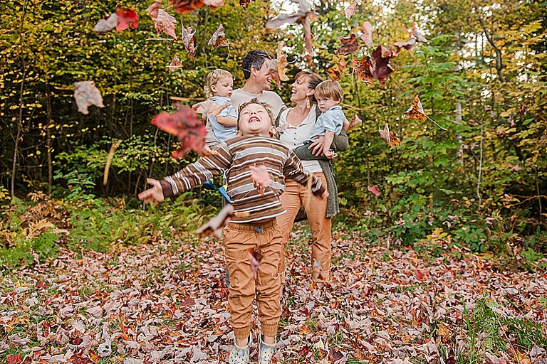 young boy throwing fall leaves in Vermont during his  burlington family photography session while his family watches