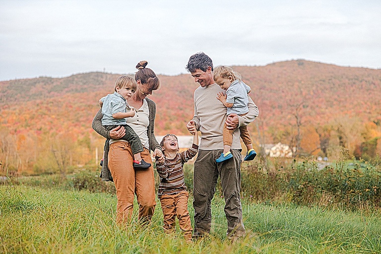 young Vermont family smiling at each other during their burlington family photography session with beautiful fall foliage as the background