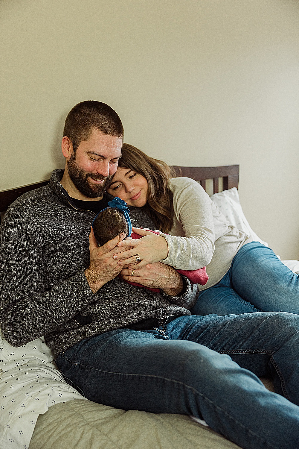 two Vermont parents cuddle and smile with their newborn baby on their bed