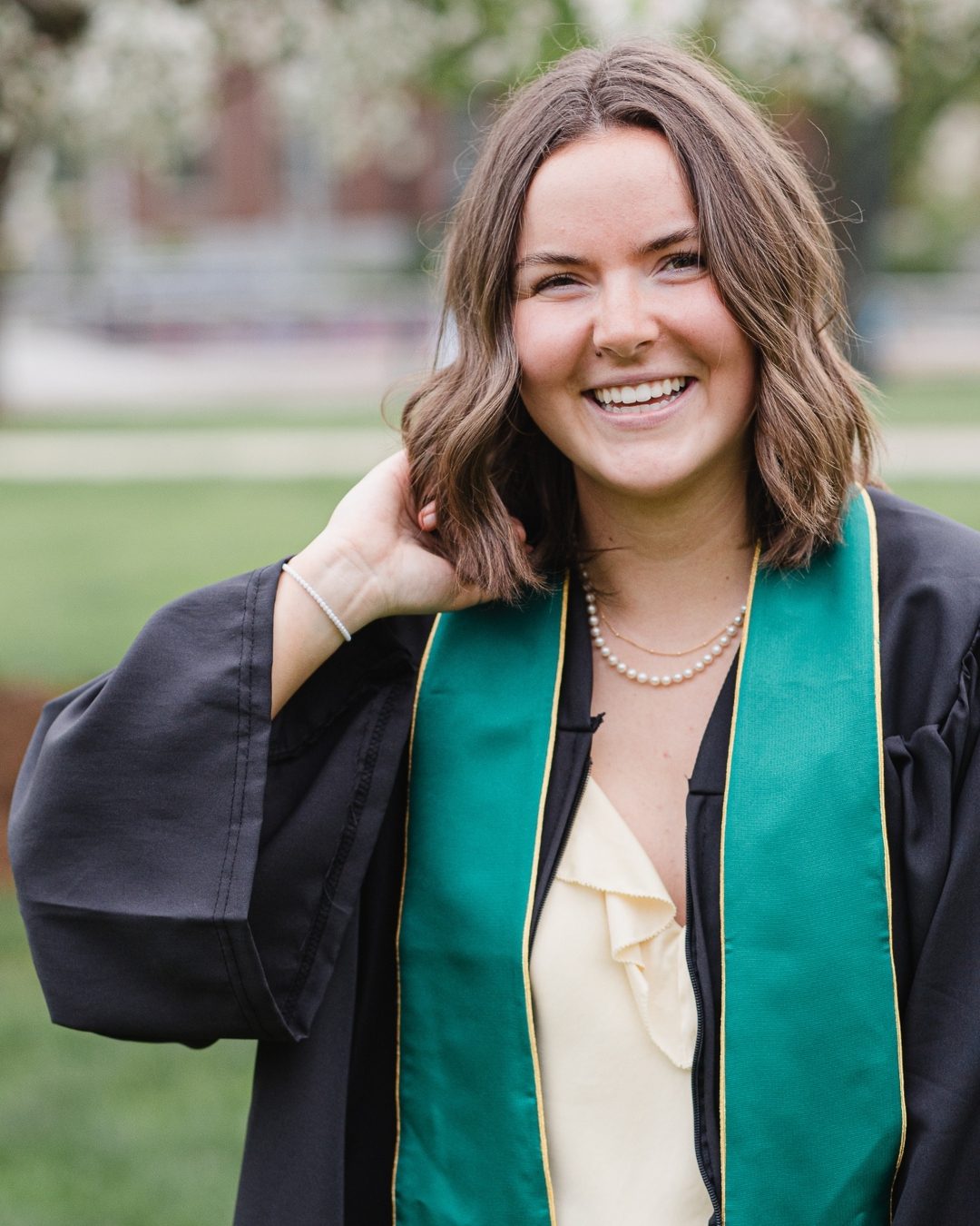 UVM senior wearing graduation gown while smiling walking around the Vermont University campus