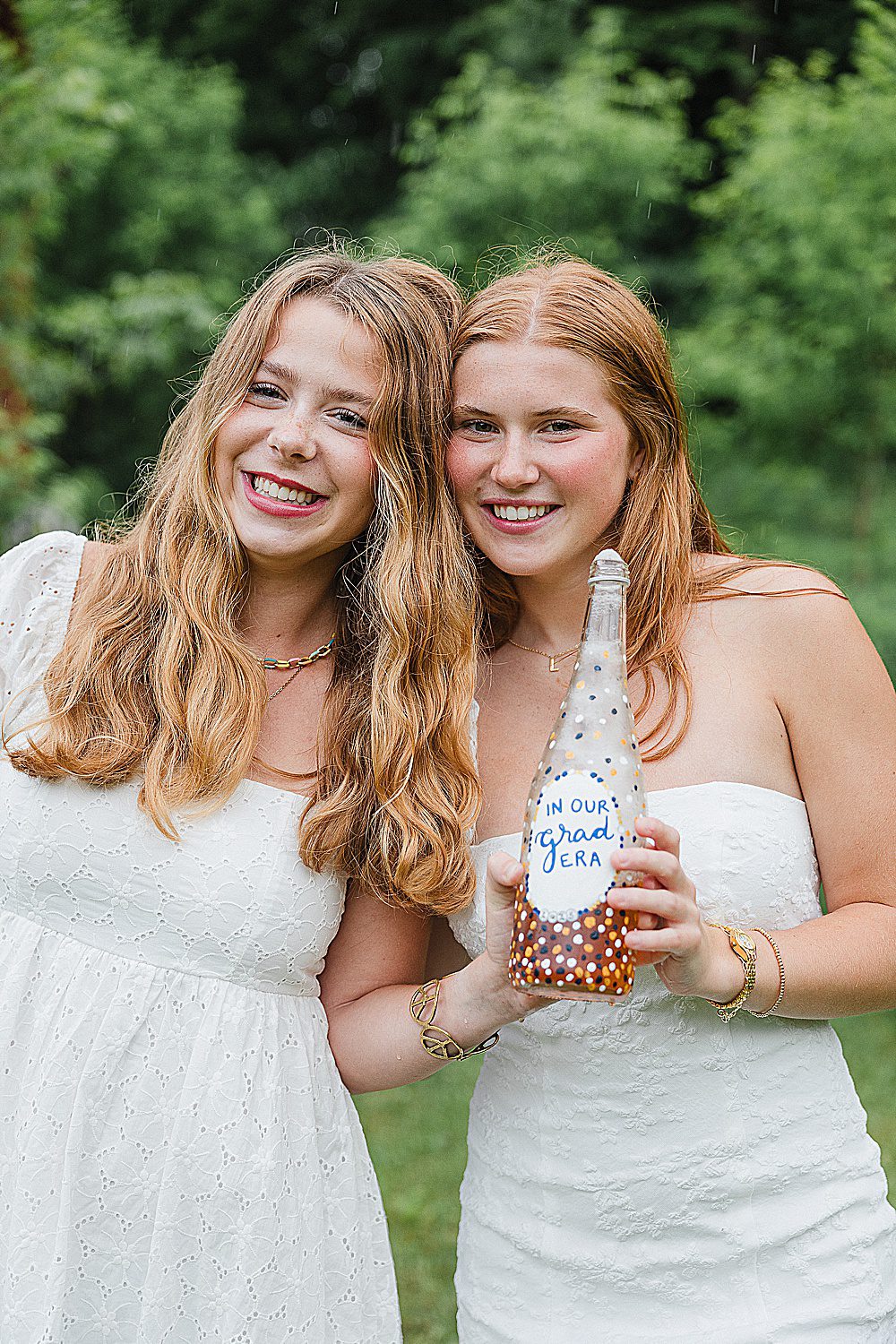 two Vermont senior girls dressed in white smiling at the camera with a bottle of Toast in their hands