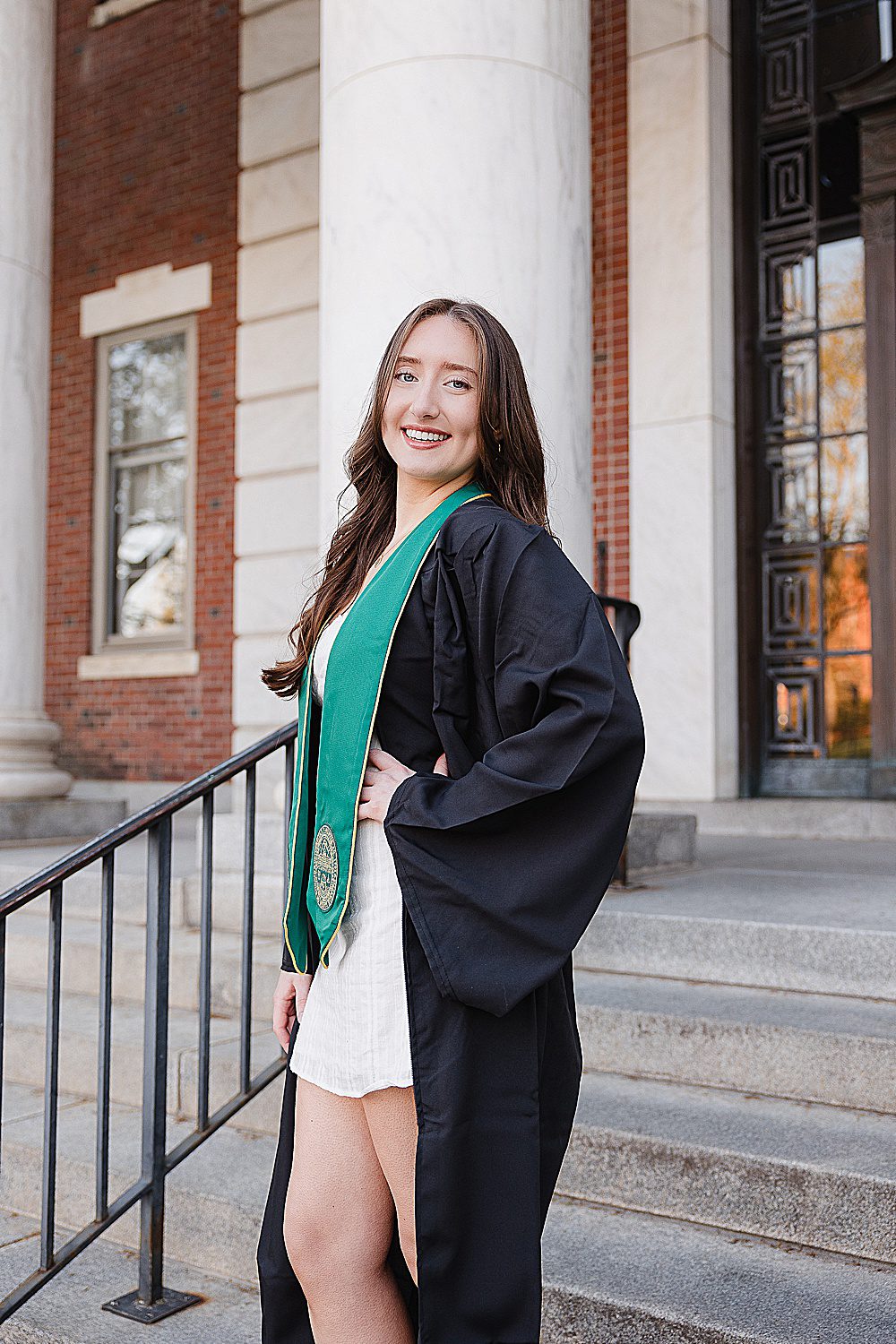 UVM Senior girl posing with her hand on her hip wearing her cap and gown