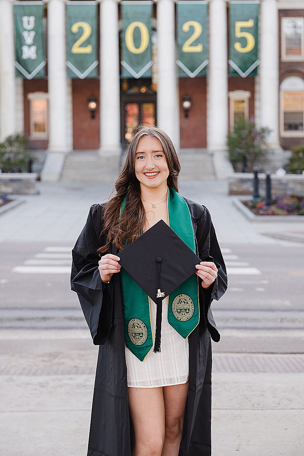 Univ. of Vermont senior smiling holding her cap with a graduation banner behind her