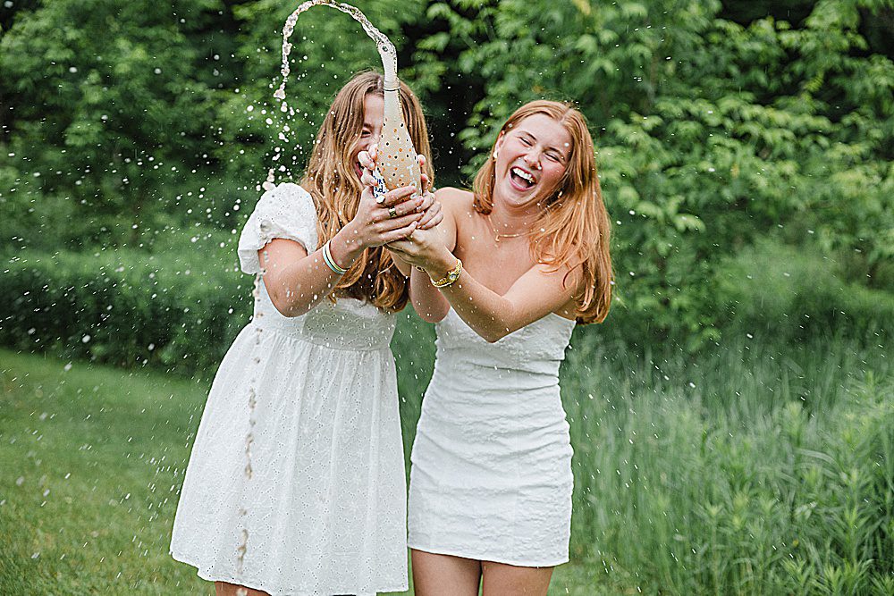 two senior friends laughing as they open a bottle of champagne, the liquid spraying out all over