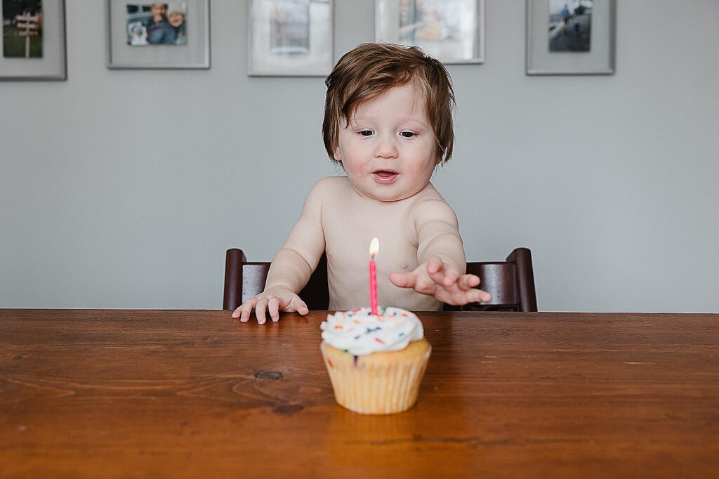 Baby turning one reaching for his birthday cake